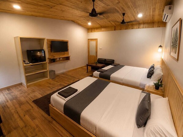A room with two beds, a television, a desk, and a ceiling fan.