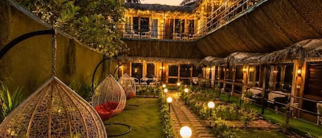 A courtyard with hanging chairs, a thatched-roof building, and a paved walkway.