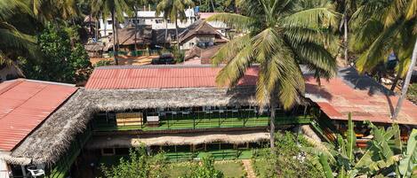 A thatched-roof structure with a green lawn, surrounded by palm trees and a mountainous backdrop.