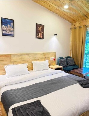 A hotel room with a wooden headboard, a bed with white bedding, a nightstand with a lamp, a green chair, and a window with curtains.