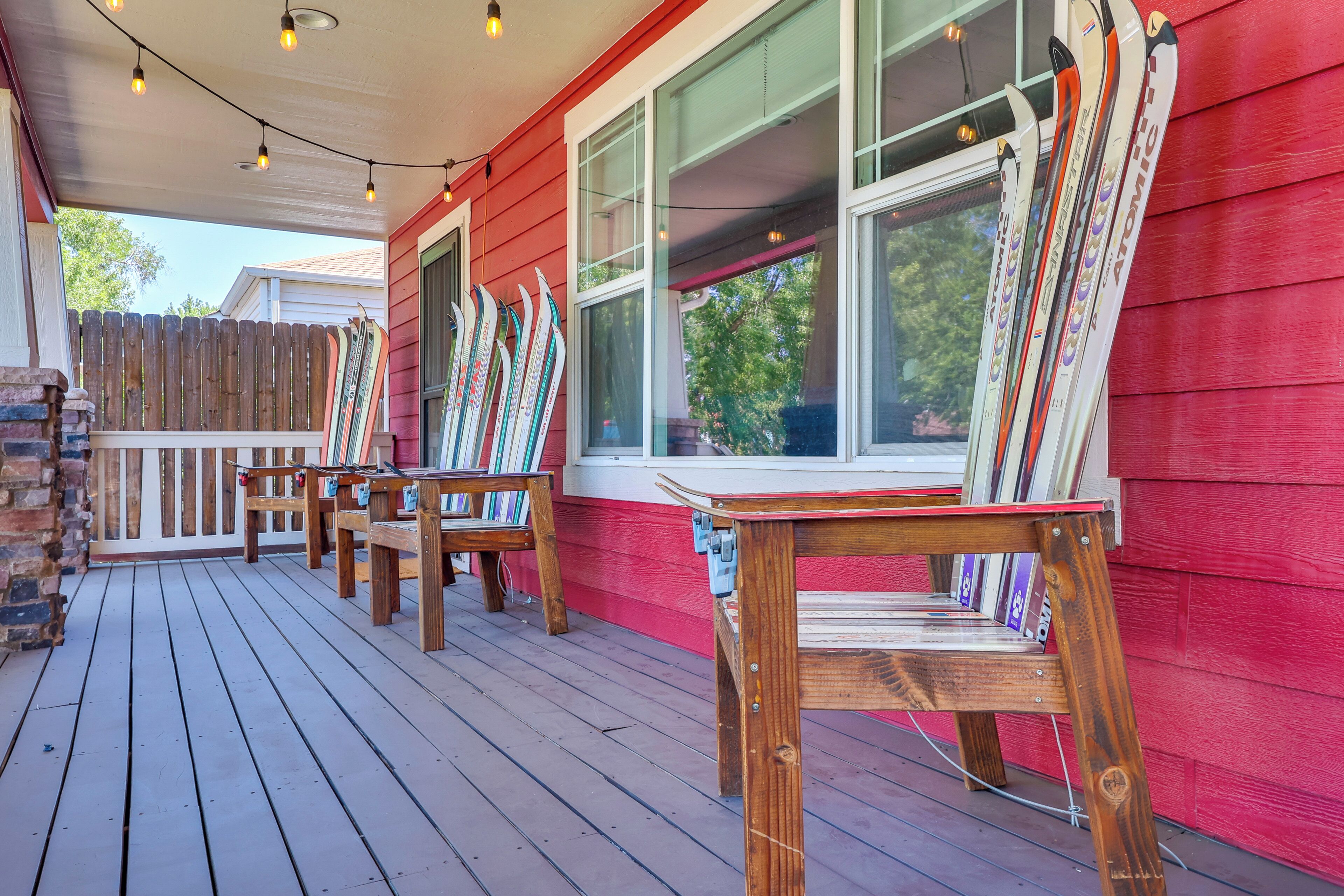 A wooden deck with benches and skis leaning against a red building.