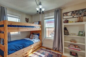 A bunk bed room with a chandelier, a bookshelf with books and games, and a window with curtains. - Historic Downtown Castle Rock Home (Castle Rock)