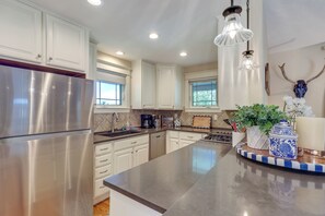 A modern kitchen with stainless steel appliances, white cabinetry, and a central island with decorative items. - Historic Downtown Castle Rock Home (Castle Rock)
