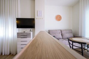 Ein modernes Wohnzimmer mit Flachbildfernseher, einem Holztisch, einem runden Esstisch, einer Couch und einer Wanduhr.