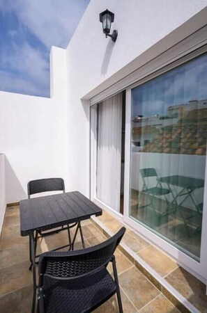 Ein Balkon mit Tisch, Stühlen, einer Schiebetür und einer Wandleuchte.