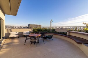 Terraço no telhado com mobiliário externo, vista panorâmica da cidade e céu limpo.