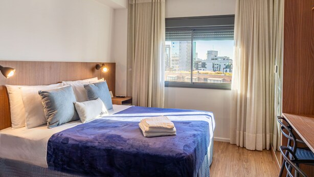 Hotellihuone, jossa on suuri sänky, työpöytä ja ikkuna, jossa on verhot.