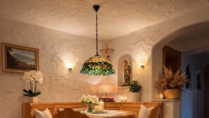 Ein Essbereich mit einem runden Holztisch, vier Stühlen, einer hängenden Leuchte aus Buntglas und einem an der Wand befestigten Kreuz.