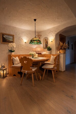 A dining area with a round wooden table, four chairs, a hanging stained glass light fixture, and a wall-mounted cross. - Relax in style in the heart of Bad Wiessee. Welcome to your getaway! (Bad Wiessee)
