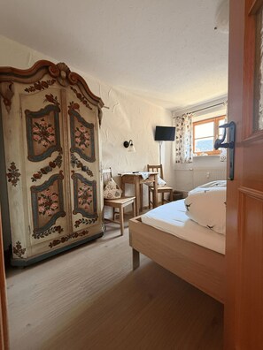 A bedroom with a bed, a wooden wardrobe, a desk, a chair, a television, and a window with curtains. - Relax in style in the heart of Bad Wiessee. Welcome to your getaway! (Bad Wiessee)