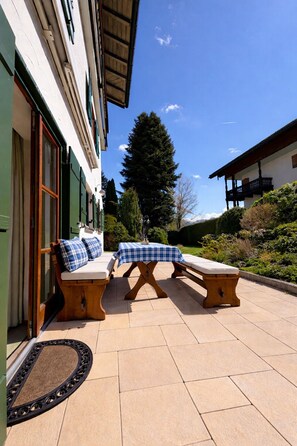An outdoor seating area with two wooden benches and a table, a doormat, and a building with a green door and windows. - Relax in style in the heart of Bad Wiessee. Welcome to your getaway! (Bad Wiessee)