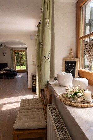 A cozy room with a bench, a radiator, a window with curtains, a bedside table with a heart-shaped decoration, and a view of an outdoor area. - Relax in style in the heart of Bad Wiessee. Welcome to your getaway! (Bad Wiessee)