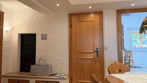 Ein Zimmer mit Holztür, einem Tisch mit Stühlen, einer Bank mit Handtasche und einer Wand mit strukturierter Oberfläche.