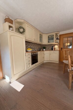 A kitchen with cream-colored cabinets, a wooden floor, and a dining area with a wooden chair. - Relax in style in the heart of Bad Wiessee. Welcome to your getaway! (Bad Wiessee)