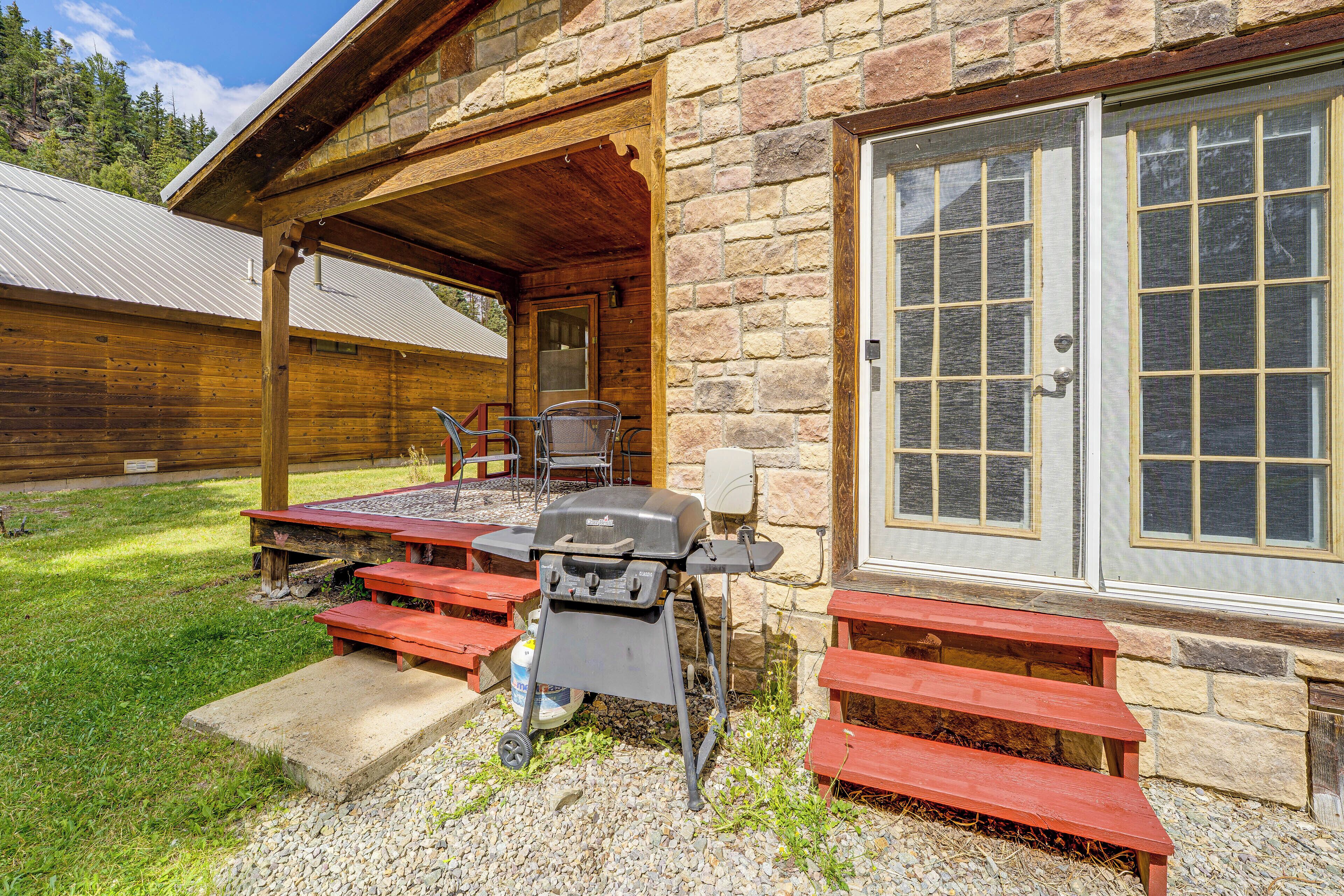 A wooden cabin with a covered patio, a barbecue grill, and a stone door.