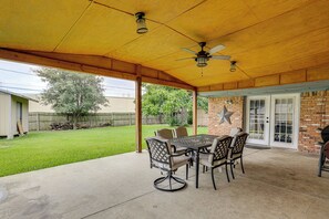 A covered patio with a table and chairs, a ceiling fan, and a brick wall with a star decoration. - Suburban Family Home Between Dallas & Arlington (Grand Prairie)