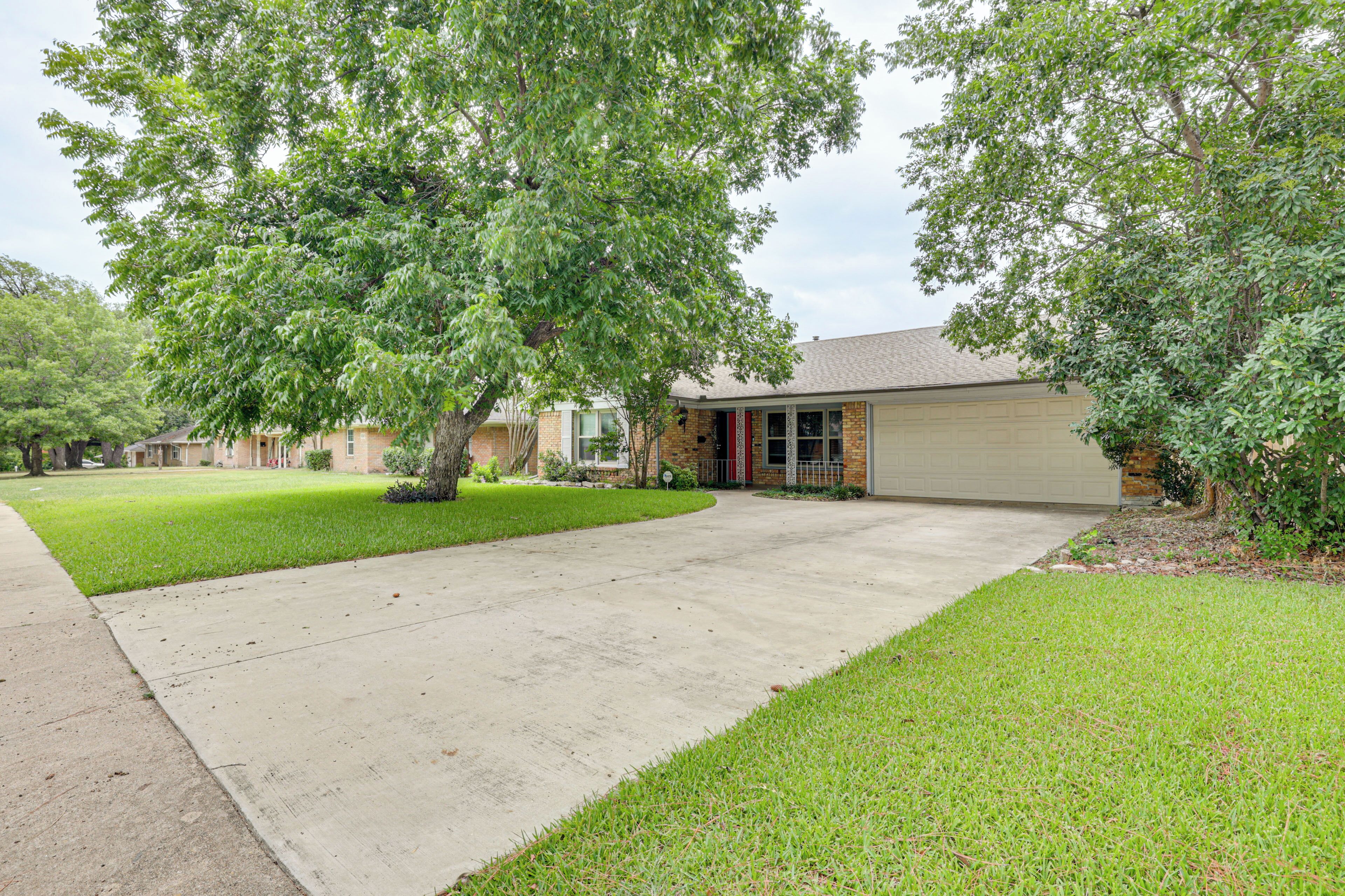 A residential property with a paved driveway, a brick house, and a well-maintained lawn.