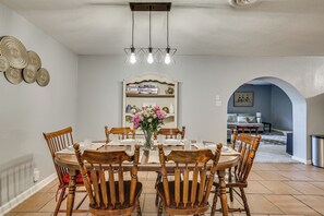 A dining area with a round table, wooden chairs, a vase of flowers, and a bookshelf in the background. - Suburban Family Home Between Dallas & Arlington (Grand Prairie)