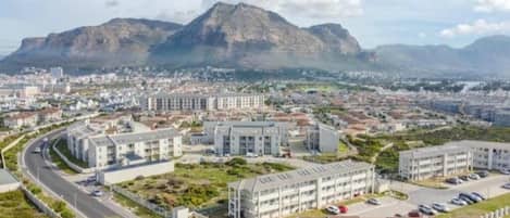 Paisagem urbana com uma montanha imponente ao fundo, edifícios modernos e uma estrada sinuosa.