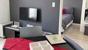 Ein modernes Zimmer mit Flachbildfernseher, Schreibtisch und einem Bett mit roter Tagesdecke.