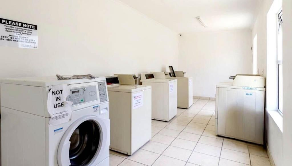 A laundry room with multiple washing machines and dryers, a sign indicating the machines are not in use, and a tiled floor.