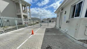 A paved entrance with a gated driveway, a building with a balcony, and a clear sky.