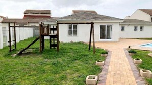 Ein Wohnhaus mit gepflastertem Weg, einer Holz-Spielanlage und einem Schwimmbecken.