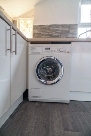 A compact, modern washing machine in a residential laundry room with a minimalist design, featuring a control panel with various settings and a stainless steel door. - Family & Contractor Stay | Sleeps 6 | Free Parking (Gateshead)
