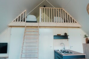 Ein Schlafzimmer im Loft-Stil mit einer Holztreppe, einer kleinen Küchenzeile und einem Balkon mit Geländer.