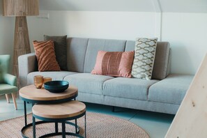 Ein modernes Wohnzimmer mit einem grauen Sofa, zwei runden Holztischen und einem gemusterten Teppich.