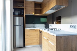 Eine moderne Küche mit Holzschränken, einem Edelstahlkühlschrank, einem integrierten Geschirrspüler, einem Gasherd und einer schwarzen Mikrowelle.