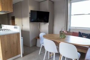 Eine kompakte Küche mit integriertem Gaskochfeld, einem Wand-Fernseher und einem Essbereich mit Holztisch und weißen Stühlen.
