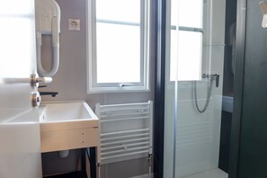Ein Badezimmer mit einem weißen Waschbecken, einem Spiegel, einem Fenster und einer Duschkabine.
