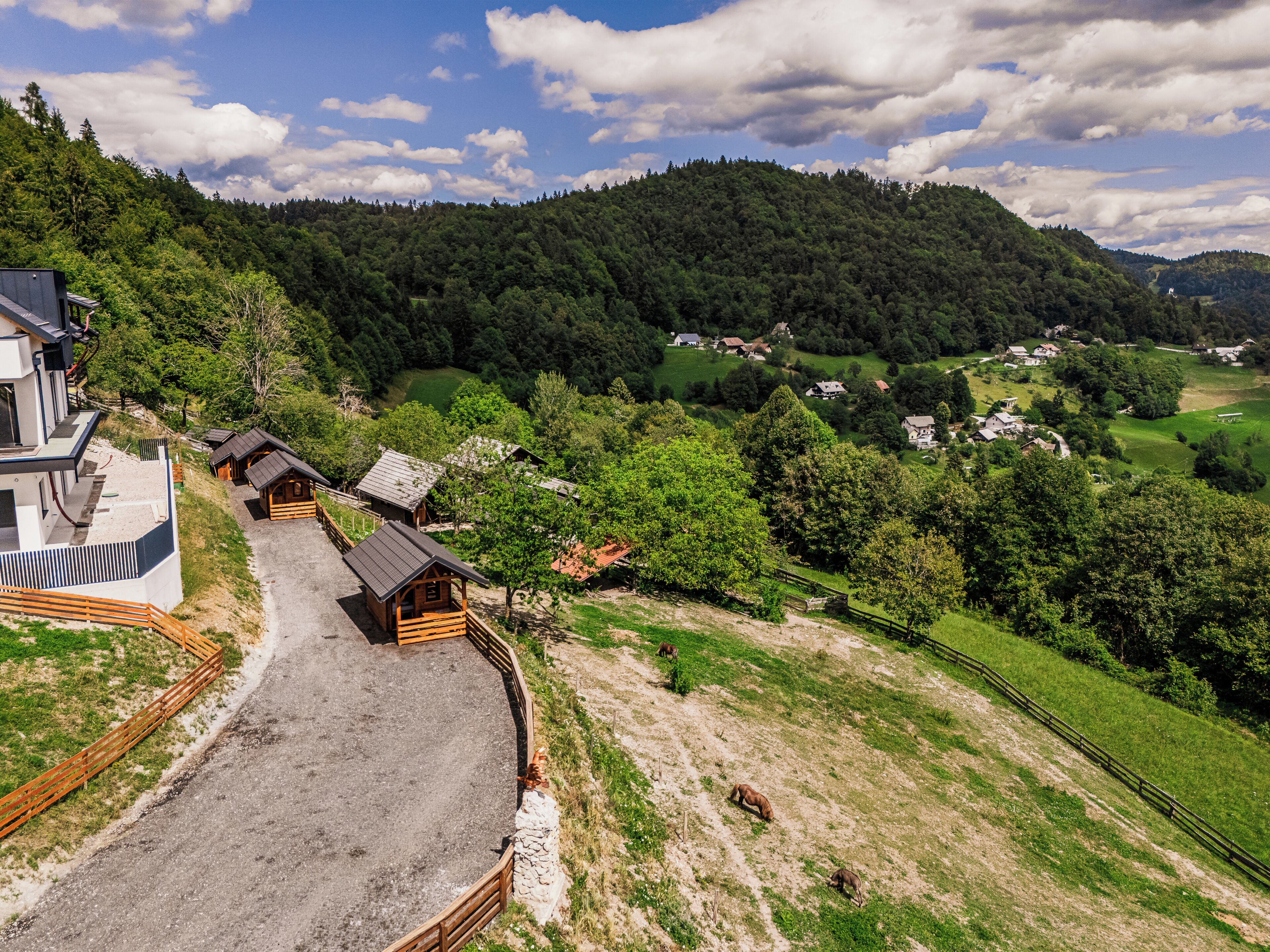 Un paisaje rural con un edificio moderno, cabañas de madera y un terreno montañoso.