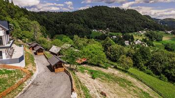 Un paisaje rural con un edificio moderno, cabañas de madera y un terreno montañoso.