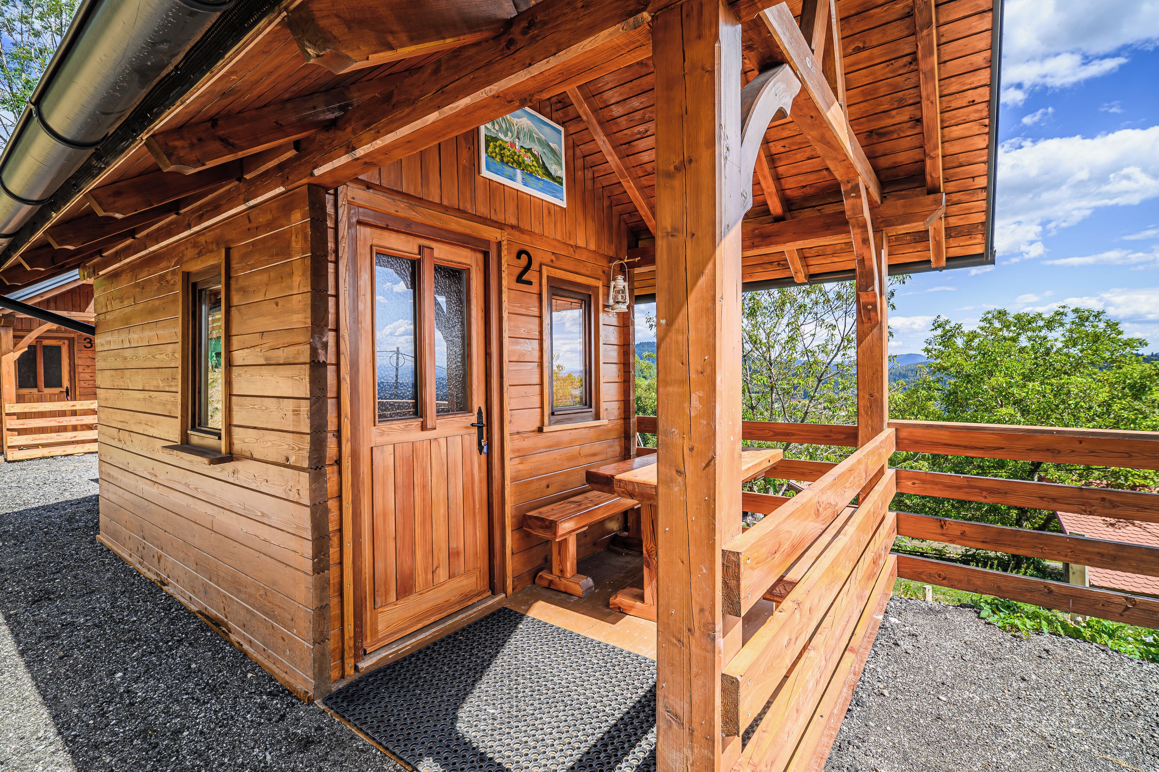 A wooden cabin with a number 2 sign, a porch with benches, and a view of the surrounding landscape.