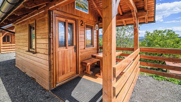 Una cabaña de madera con un letrero con el número 2, un porche con bancos y vistas del paisaje circundante.