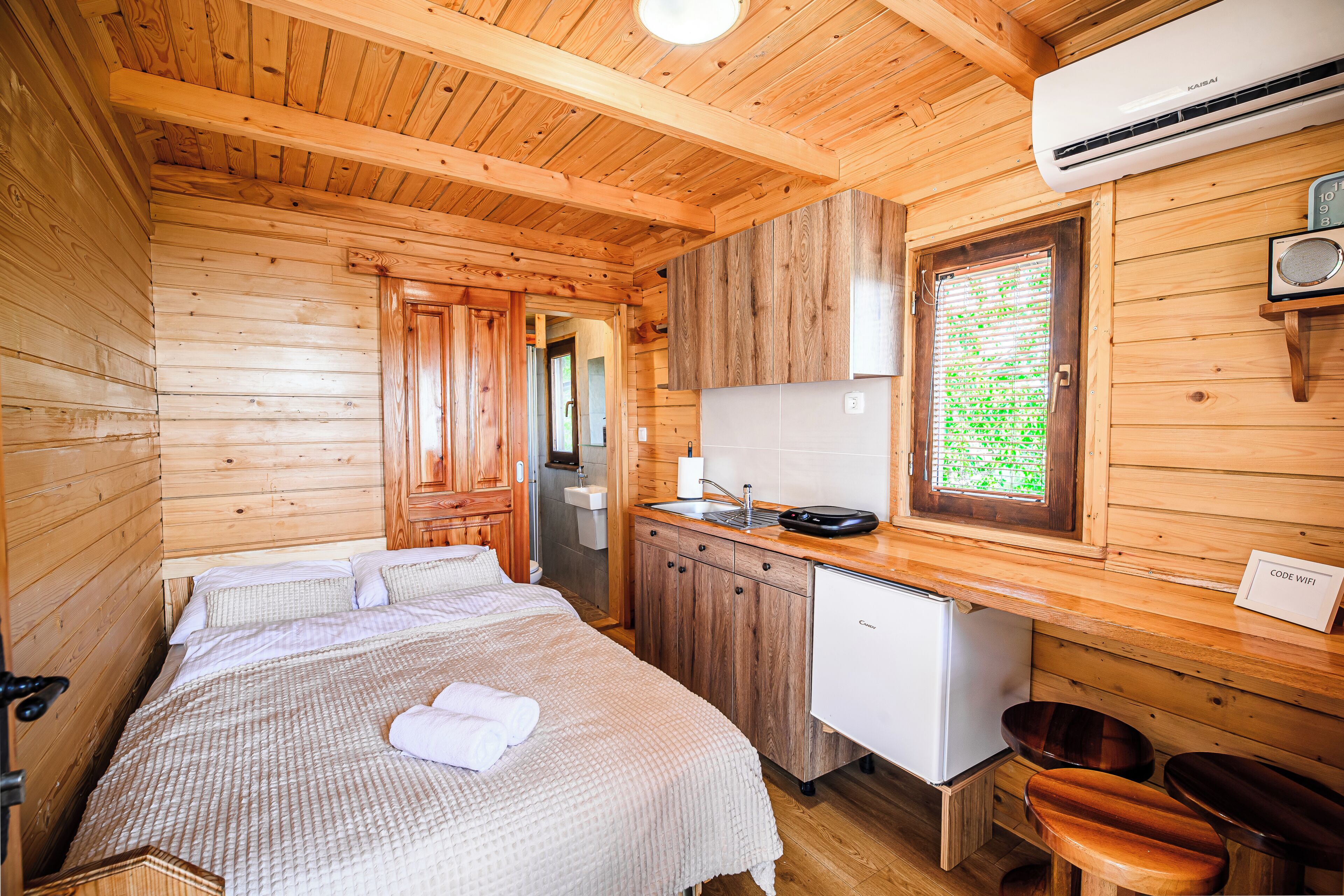 A wooden cabin interior with a bed, kitchenette, and a small refrigerator.