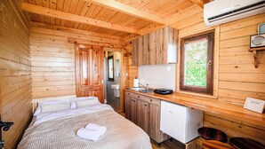 Interior de una cabaña de madera con cama, kitchenette y un refrigerador pequeño.