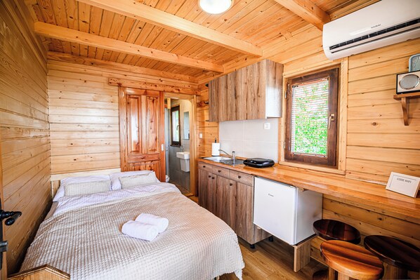 A wooden cabin interior with a bed, kitchenette, and a small refrigerator. - Tiny Panorama Cottages (Kamnik)