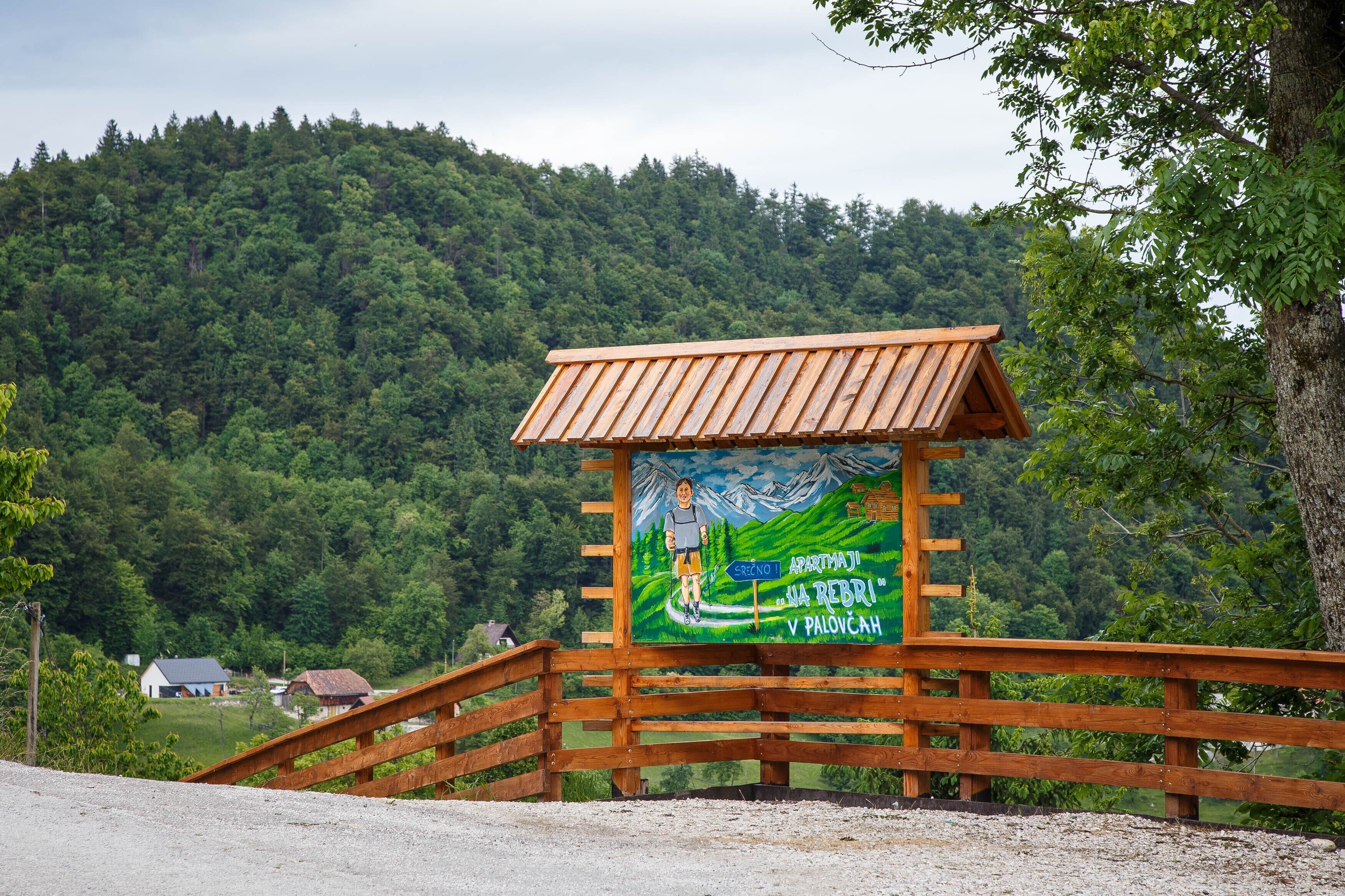 A wooden sign with a painted landscape, a directional arrow, and text indicating a location.