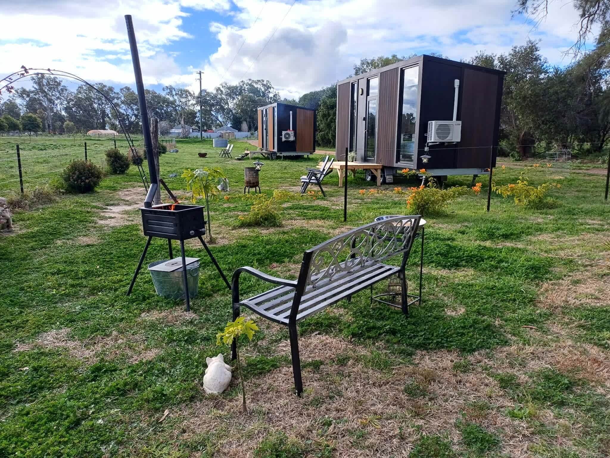 A grassy outdoor area with a bench, a portable stove, and a trailer with a kitchen area.