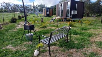 A grassy outdoor area with a bench, a portable stove, and a trailer with a kitchen area.