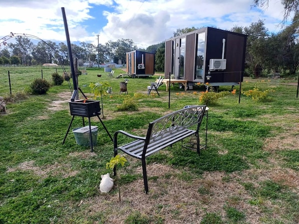 A grassy outdoor area with a bench, a portable stove, and a trailer with a kitchen area.
