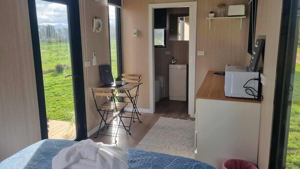 A compact room with a bed, a small table, a chair, a kitchenette, and a view of the outdoors. - The Druids Rest by Tiny Away (Curlwaa)
