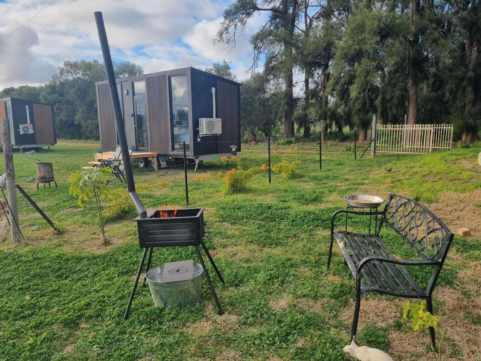 A grassy outdoor area with a portable grill, a bench, and two mobile homes.