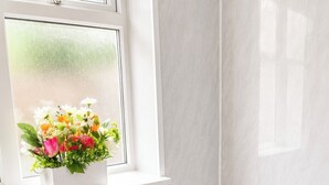 Et badeværelse med toilet, hvid radiator og et vindue med blomsterarrangement.