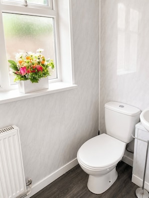 A bathroom with a toilet, a white radiator, and a window with a flower arrangement. - Room-cosy Room in Wolverhampton Perfect (Wolverhampton)