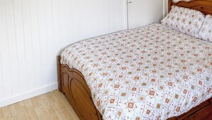 Et soveværelse med en træseng, et hvidt skab, et lille vindue med rødt gardin og en lampe i loftet.
