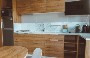 Eine moderne Küche mit Holdekor, einem Edelstahlkühlschrank, einem Gasherd, einer Spüle und einem flachen schwarzen Flachbildfernseher, der über der Arbeitsfläche angebracht ist.